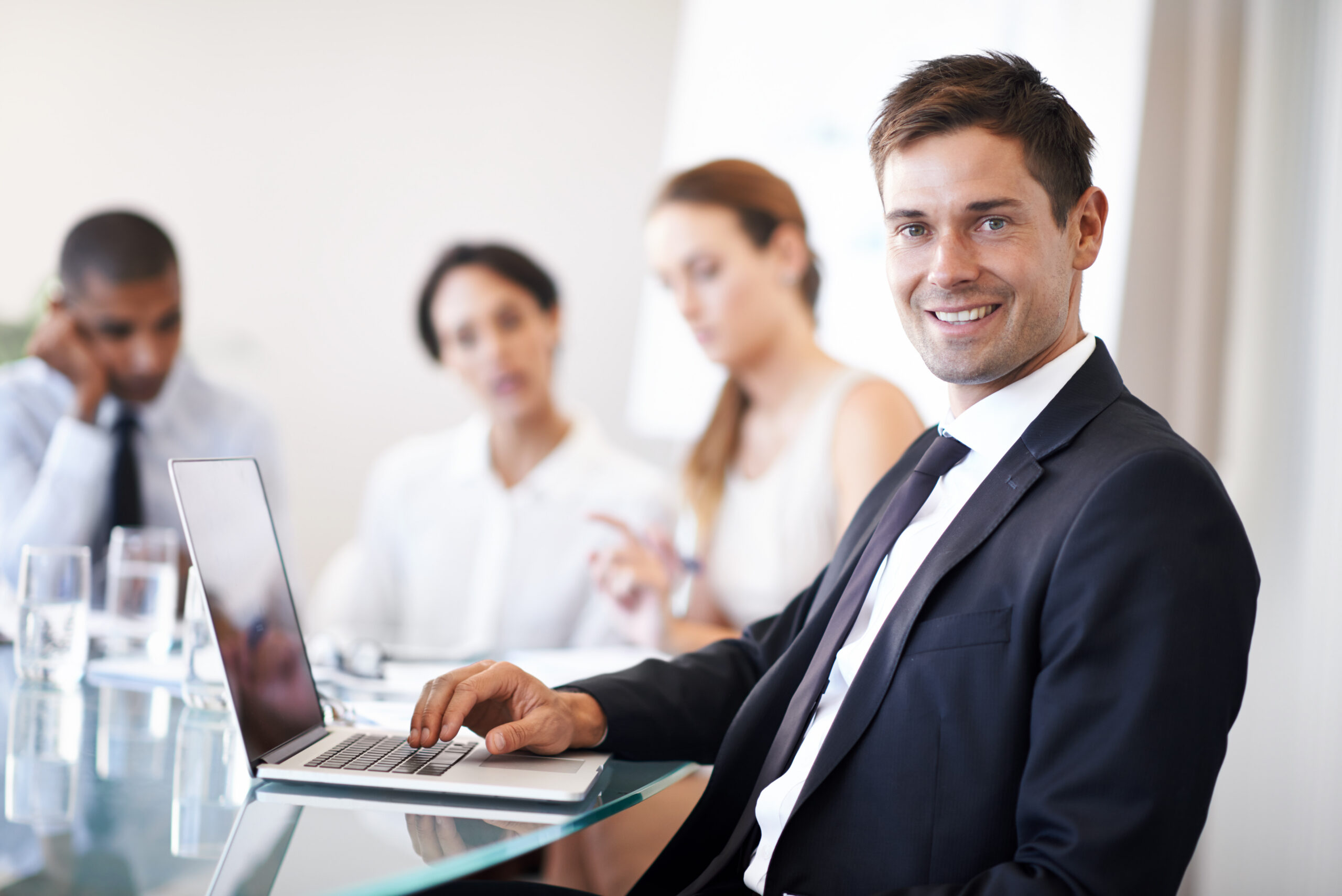 A business professional smiling confidently with his team discussing in the background.