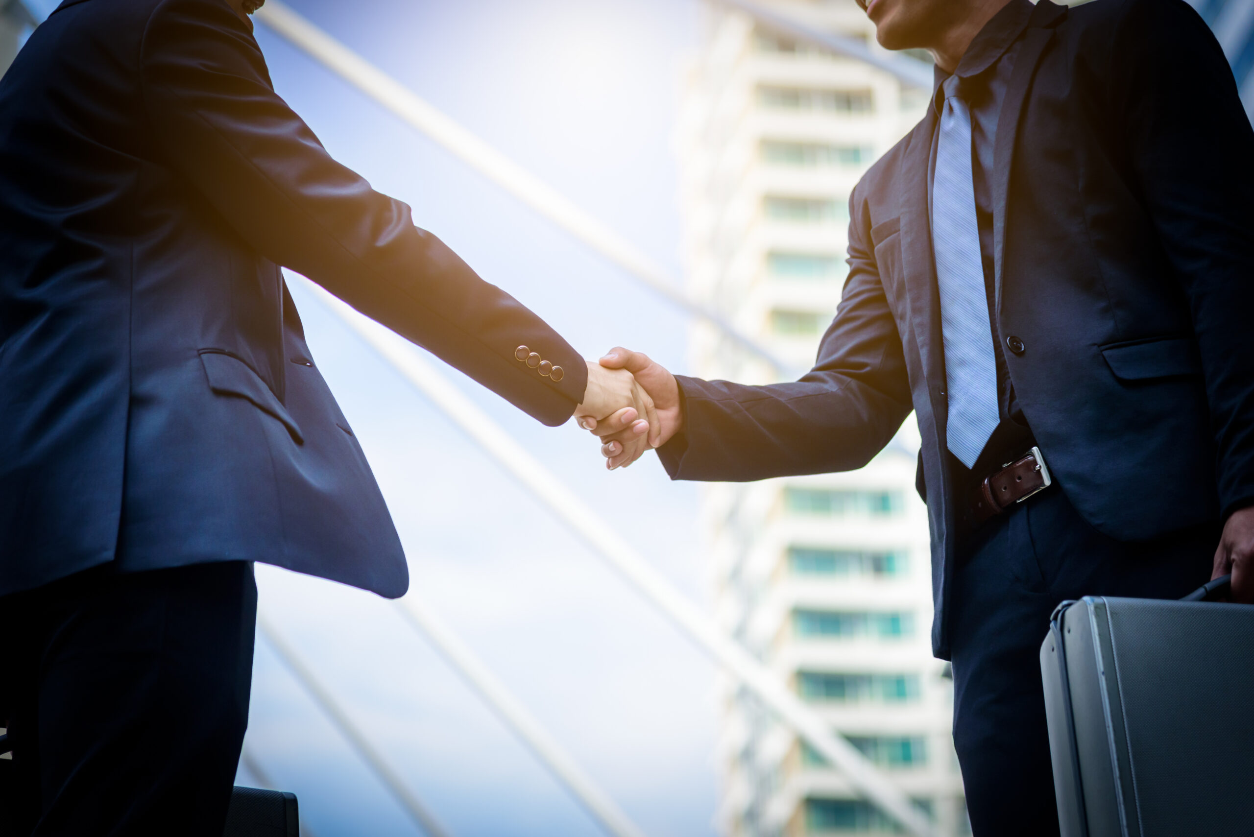 Two business professionals shaking hands outside an office.