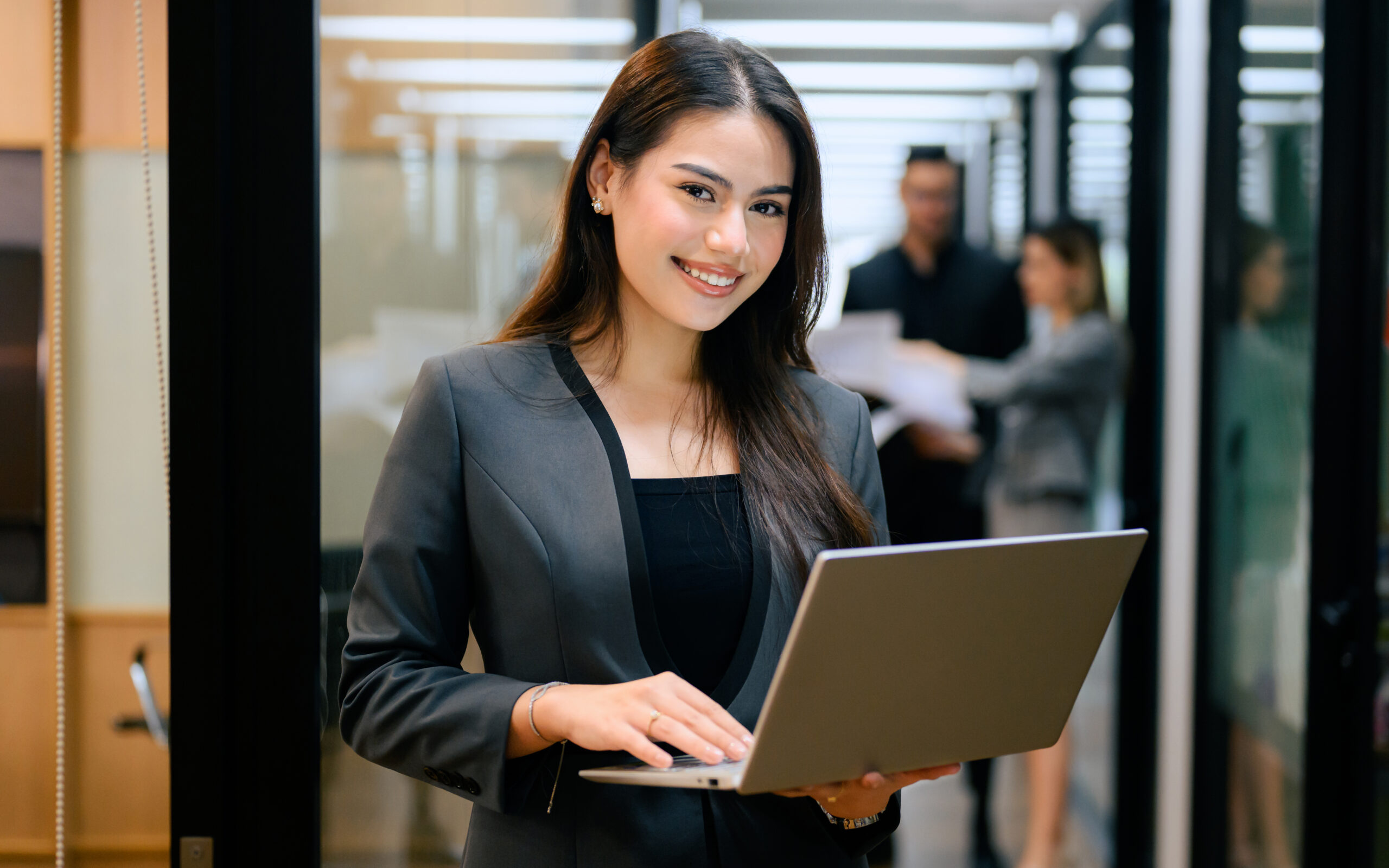 A smiling young professional standing while holding a laptop