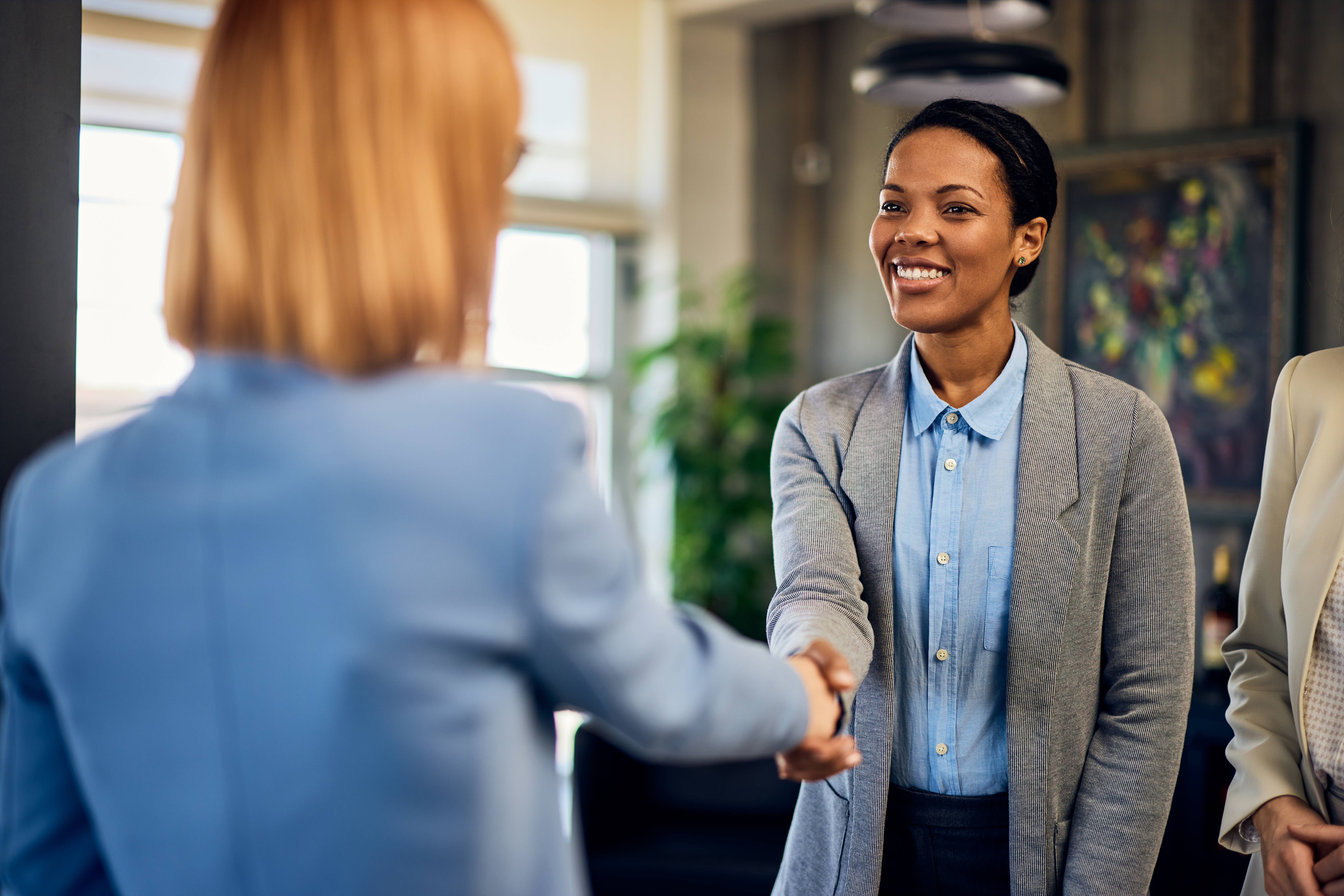 A young business professional shaking hands with her client in a modern office setting.